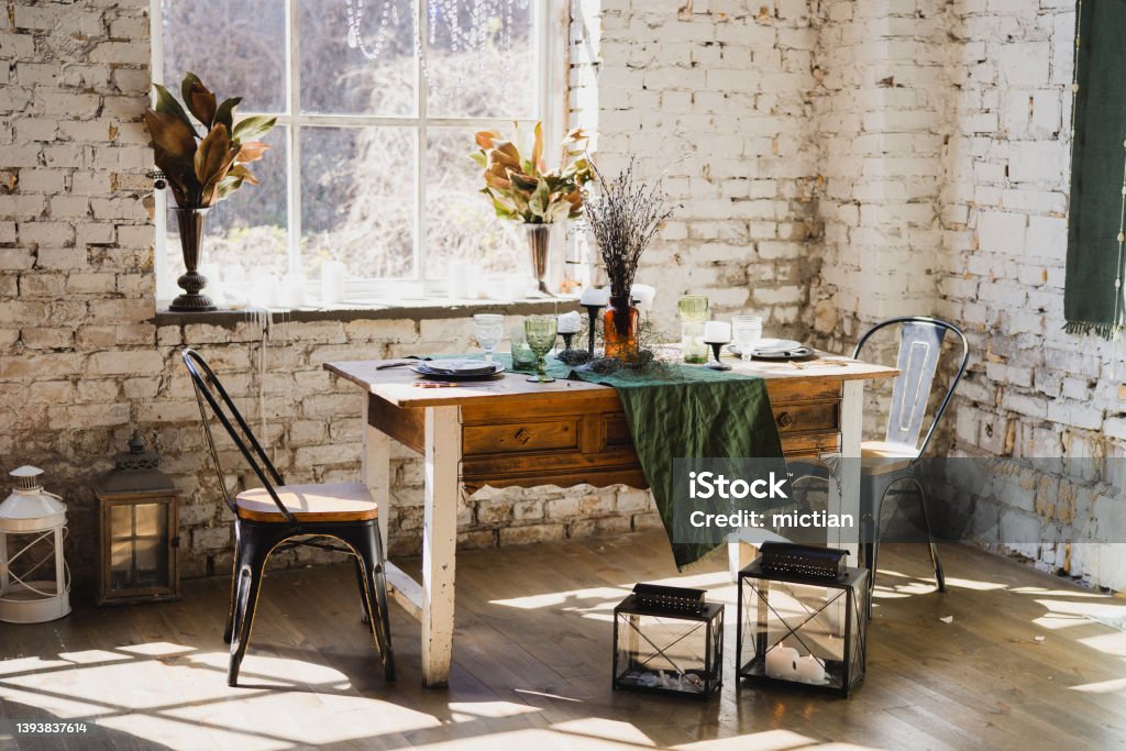 Beautiful vintage dining table with decorations, flowers, candles and laying near the window. Coziness at home. Modern interior design. Loft, botanic, rustic style. Table set for an event, party, date or wedding. Dinner Stock Photo