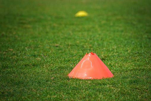 An orange obstacle cone which is using for movement and speed practice, it placed on football training grass pitch.