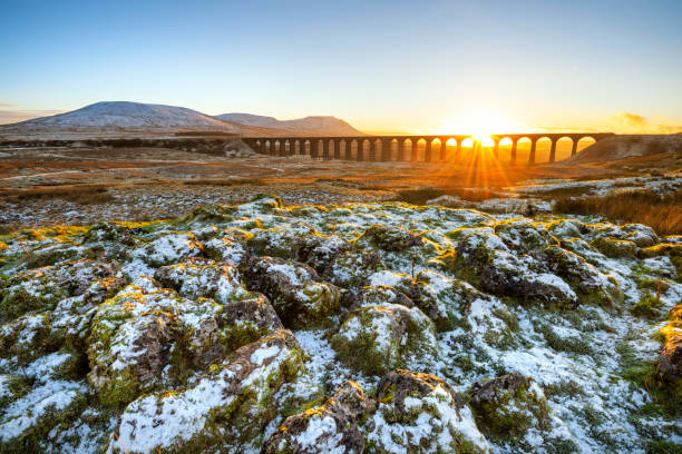 Ribblehead Viaduct Sunset, Yorkshire Dales, UK. Golden light on a cold Winter evening at Ribblehead Viaduct in North Yorkshire with snow covered rocks in foreground. ingleborough stock pictures, royalty-free photos & images