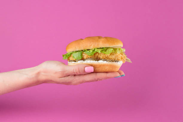 istock Female hand with tasty burger on pink background 1393842917