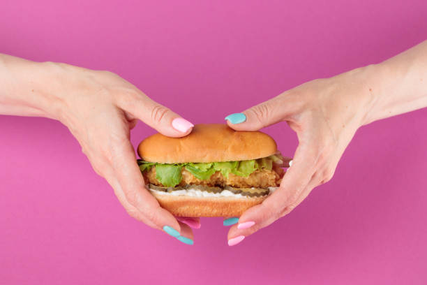 istock Female hand with tasty burger on pink background 1393842953