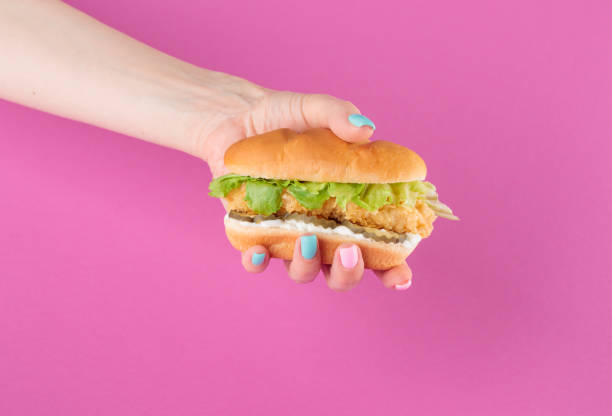 istock Female hand with tasty burger on pink background 1393842974