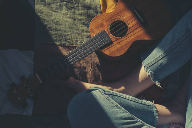 Woman musician with ukulele sitting at patchwork quilt.