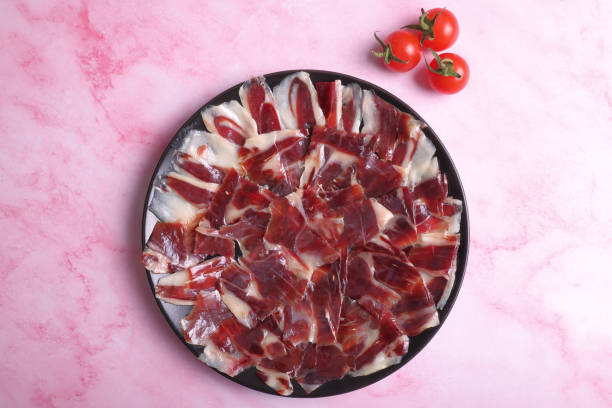 Portion of 100% Iberian ham of dehesa de Extremadura acorn decorated with tomatoes on a marble pink background Ration of 100% Iberian acorn-fed ham Dehesa de Extremadura decorated with tomatoes on a pink marble background acorn photos stock pictures, royalty-free photos & images