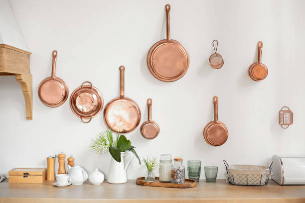 Different kind of cookware and ceramic plates on tabletop wooden kitchen. Set of copper saucepans, pans, pots and ladle hanging in kitchen. Hanging kitchen utensil on wall. kitchen interior decor