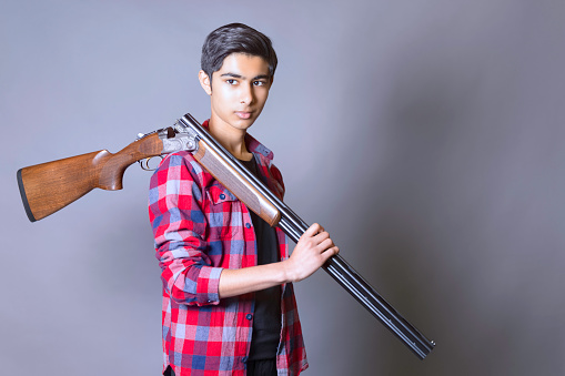 Teenaged youth of Indian heritage carrying a shotgun.