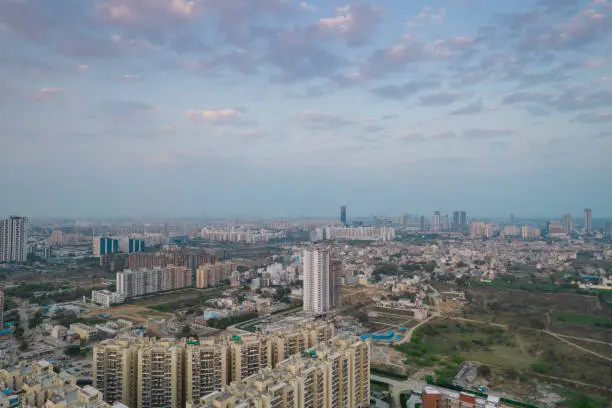 aerial drone shot passing over a building with homes, offices, shopping centers moving towards skyscapers in front of sunset showing the empty outskirts of the city of gurgaon India Asia
