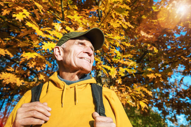 elder hiker with smile and with backpack standing against oak tree leaves - autumn sun oak tree imagens e fotografias de stock