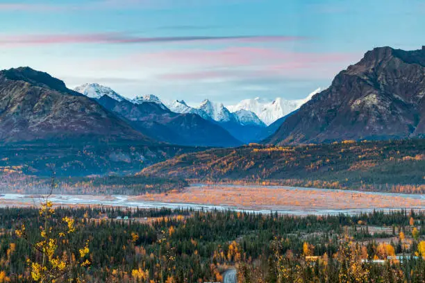 Photo of dramatic landscape of golden yellow autumn foliage of aspen and birch trees and snowcapped mountains of the Chugach mountain range in Alaska.