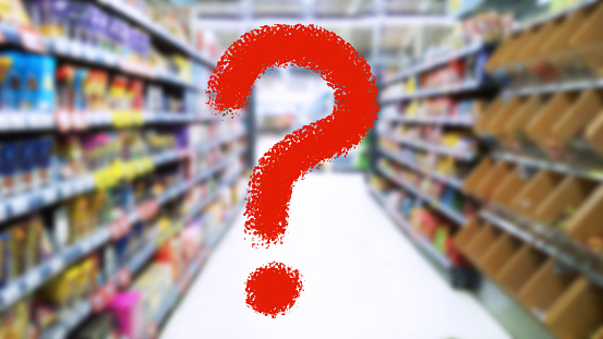 Large red question mark on blur supermarket background. Defocused shelves with food products. Grocery Store. Retail industry. Rack. Inflation and economic crisis concept. Supply chain issues. Business