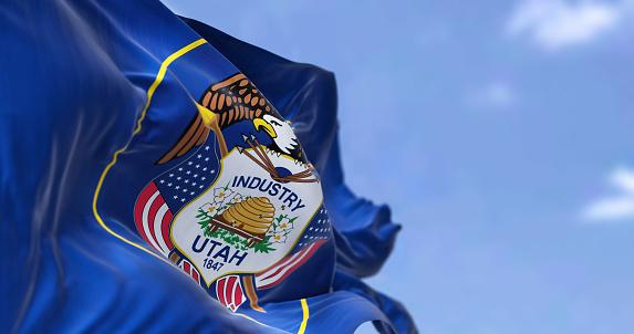 The US state flag of Utah waving in the wind. Utah is a state in the Mountain West subregion of the Western United States. Democracy and independence.