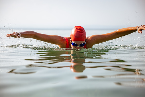 Professional triathlete swimming in river's open water. Man wearing swim equipment practicing triathlon on the beach in summer's day. Concept of healthy lifestyle, sport, action, motion and movement.