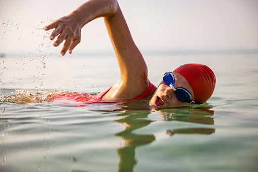 Young Caucasian woman swimming in the sea, while wear swimming goggles, swim cap and swimsuit