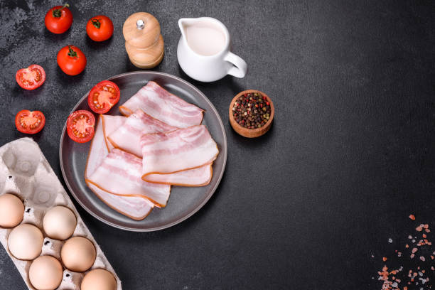 istock Delicious fresh raw bacon cut with slices on a grey plate against a dark concrete background 1393857064