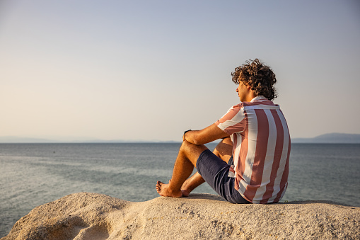 Young Caucasian man admiring the sunset from the rocky beach