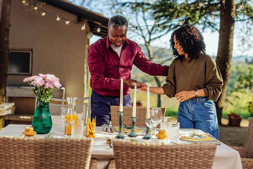 African american mid adult man and young adult woman preparing and decorating a table outside in a huge garden for a dinner party.