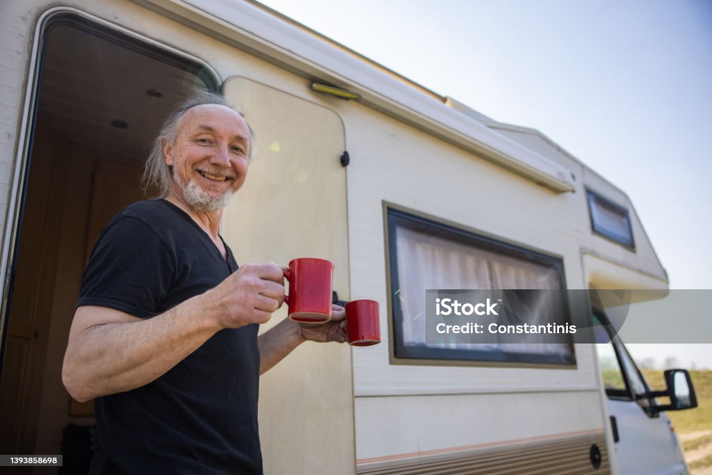 Excited man holding cup of coffee, during picnic time with hic camper van Carefree Caucasian man carrying two cup of coffee, while enjoy the adventure with his camper van 50-54 Years Stock Photo