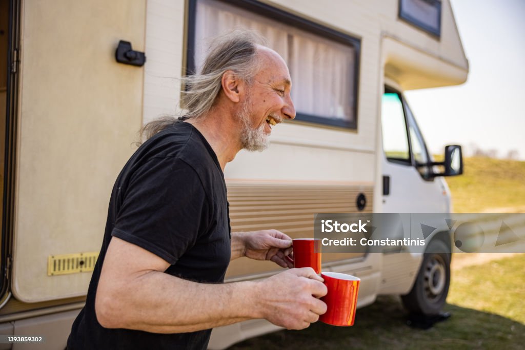Serene man holding cup of coffee, during picnic time with hic camper van Carefree Caucasian man carrying two cup of coffee, while enjoy the adventure with his camper van Car Stock Photo