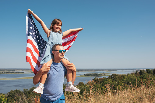 Happy family father and child with flag of united states enjoying sunset on nature. Free lifestyle concept.