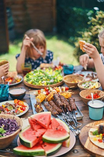 Young Family Eating Lamb, Beef and Vegetable Kebab with Green Salad Outside in the Garden