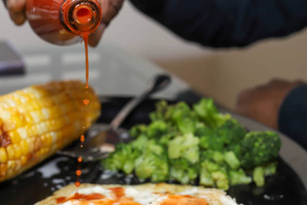 un uomo afroamericano nero che versa salsa piccante sul cibo - tabasco sauce foto e immagini stock