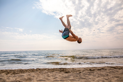 Caucasian man doing the back/front flip on the beach, during summer vacation