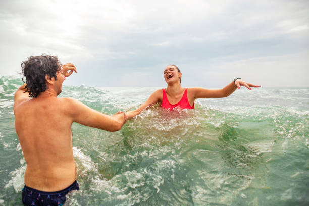 Carefree young female and male friends or siblings having fun during their vacaion, while playing in the sea while waves splashing them