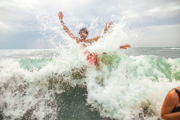 Carefree young female and male friends or siblings having fun during their vacaion, while playing in the sea while waves splashing them