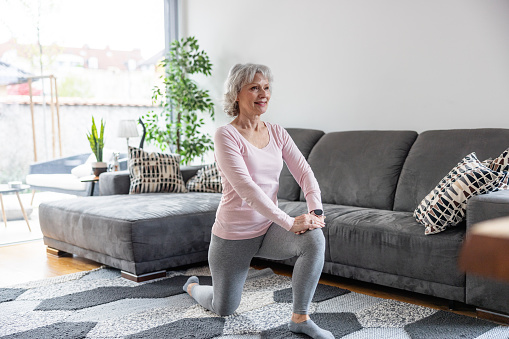Cheerful Senior Caucasian Woman Doing Lung Stretch Exercise At Home