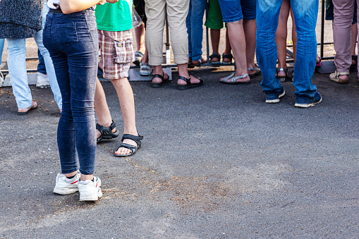 The feet of music lovers stand at an entertainment event. People stand in front of the music scene at a concert. People are standing on the sidewalk.