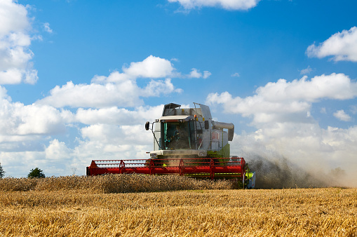 Combine harvester harvesting crops at barley field against cloudy sky during sunny day