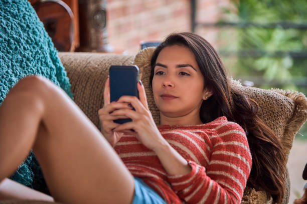 istock Hispanic young woman laying down on sofa and using smartphone 1393872023