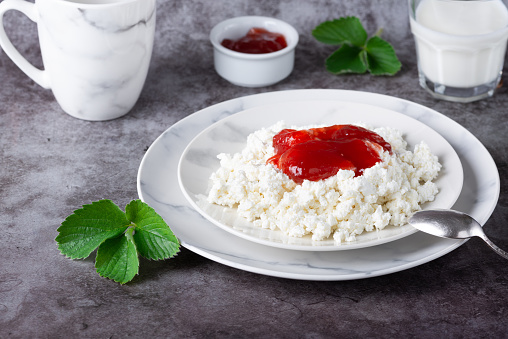 Plate with cottage cheese, strawberry jam and milk on grey table.