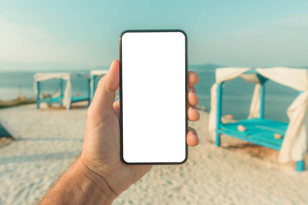 istock Mobile smart phone with blank mockup template screen in male hand, beach pergola in background 1393876049
