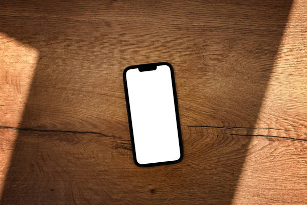 istock Smartphone with blank white mockup touchscreen on teak wooden table 1393876056