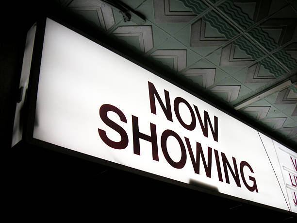 A brightly illuminated now showing sign glows at night "now showing" - neon sign advertising upcoming films @ cinema box office photos stock pictures, royalty-free photos & images