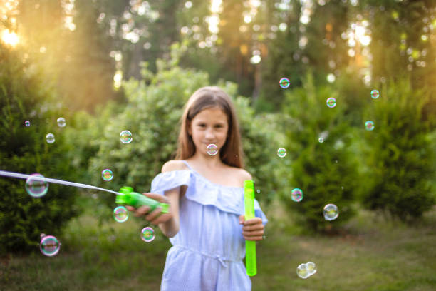 Girl launches soap bubbles on the street. Background of green trees
