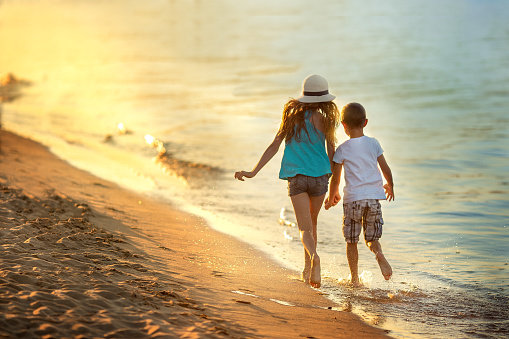 Boy and a girl run along the beach along the seashore. Summer, sunset, water splashes