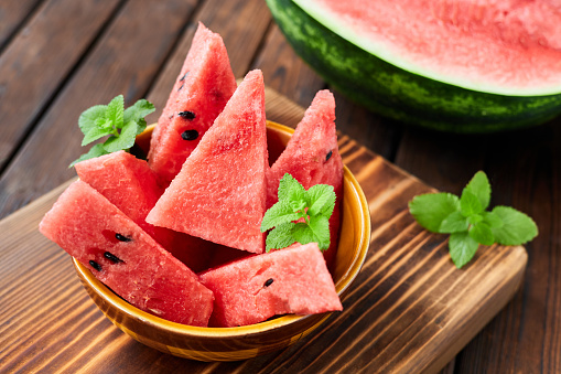 Sliced watermelon decorated with mint leaves on brown wooden background. Close-up, selective focus