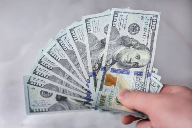 istock Banknotes of 100 dollars unfolded in a hand on a light background 1393880956