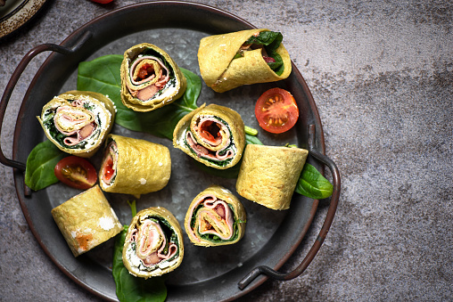Tortilla wrap with ham,cheese and tomatoes .Wrap sandwich with pink salmon,corn,and spinach in spinach wrap in bowl on gray background.Top view.