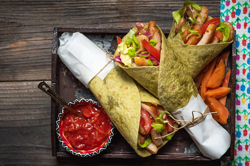 Homemade vegan tortillas, with red beans, sweet potatoes, tomatoes, guacamole in a wooden bowl with sauces and spices on a rustic wooden background. Stock photo.