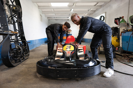 Team of Latin American mechanics working together to fix a go-cart at a race track garage