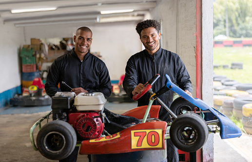 Portrait of two happy mechanics working at a garage fixing go-carts and looking at the camera smiling