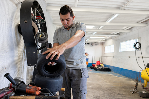 Latin American mechanic inflating a small tire from a go-cart at an Auto Repair Shop - flat tire concepts