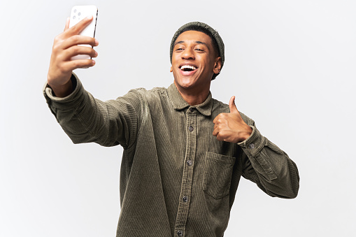 Waist up view of the young man showing big finger gesture with his hand while chatting via cell phone or making selfie, isolated on white background