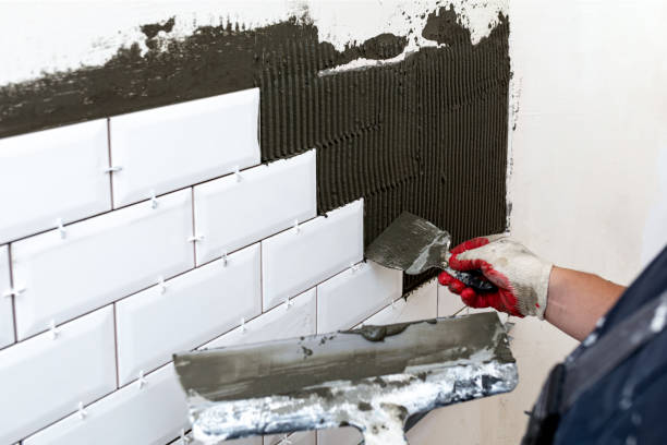 istock Wall cladding. The master's hands apply tile glue to the walls using two spatulas of different sizes. 1393889876