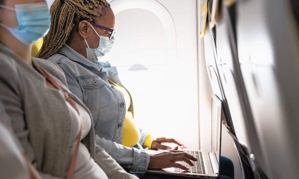 Senior woman using laptop during airplane trip while wearing face mask