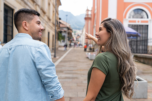 Happy Latin American couple sightseeing in Bogota and pointing away on the street  - travel concepts