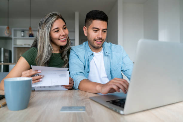 happy couple at home paying bills online - huishoudkosten stockfoto's en -beelden